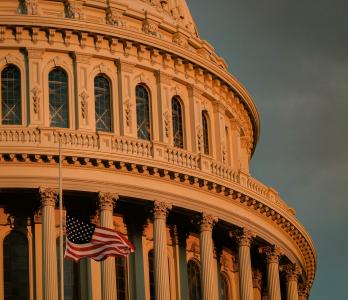 photo depicts the top of the capitol building with an American flag in the bottom left corner
