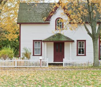 photo of a small home with a white picket fence, surrounding by autumnal foliage